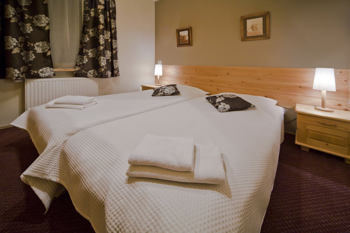 Une chambre d’hôtel avec deux lits, chacun agrémenté de draps et d’oreillers blancs, d’une tête de lit en bois, de tables de chevet avec des lampes et d’un tableau encadré au mur.