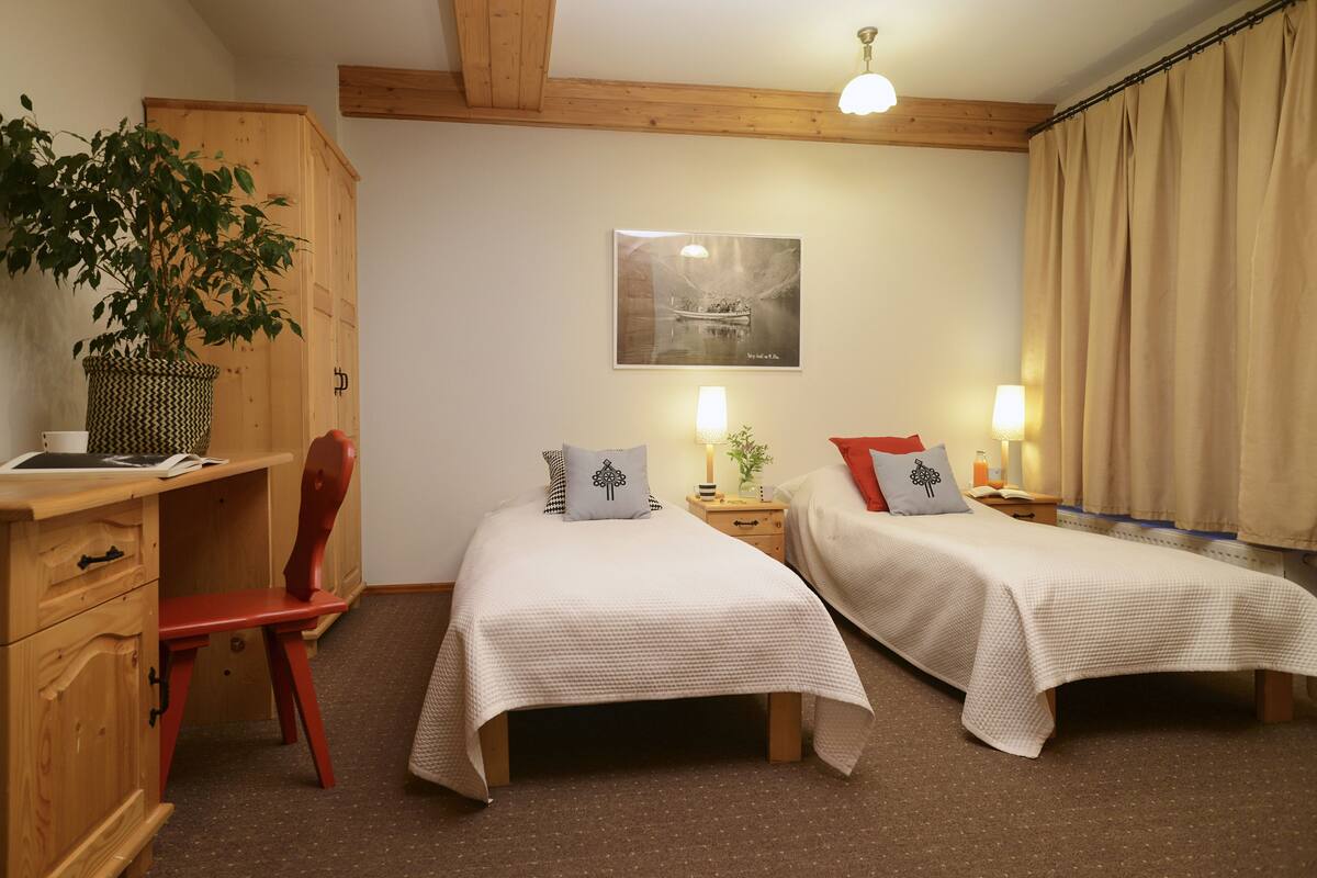Une chambre avec deux lits, un bureau, une chaise, une plante et un tableau au mur.