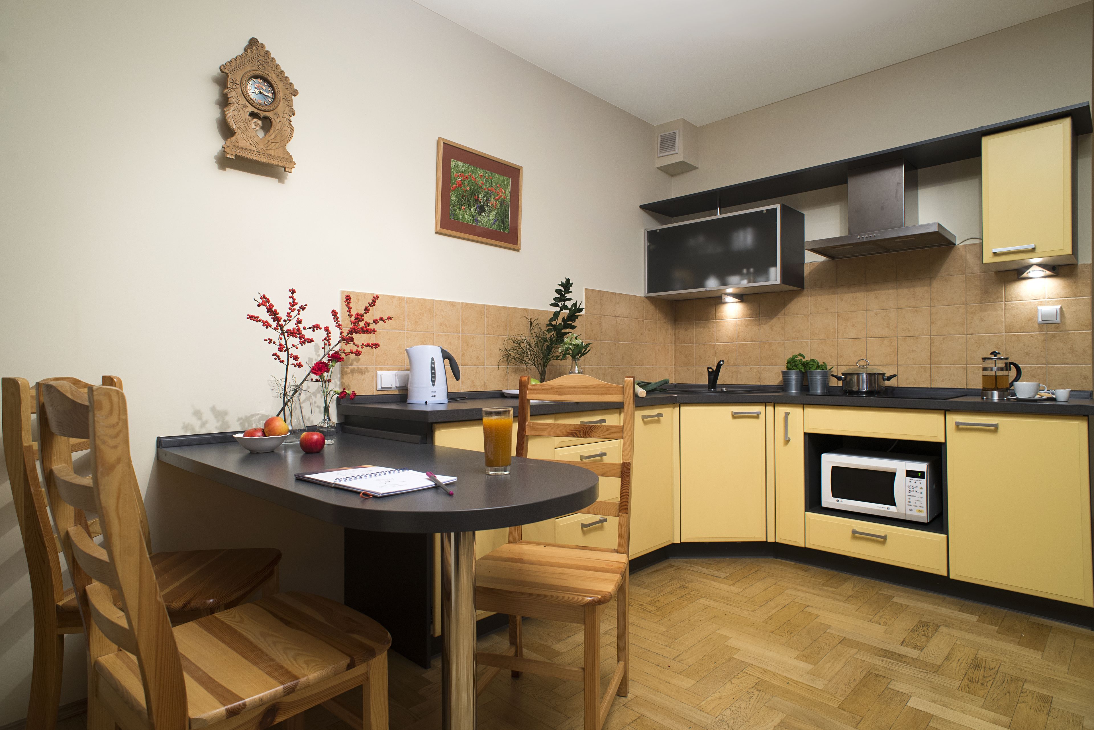 Una cocina con sillas de madera, una mesa, un microondas y un reloj en la pared.