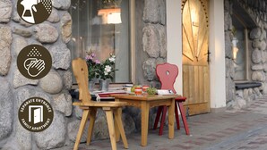 A stone wall with a wooden table and chairs, a potted plant, and a wooden door with a light fixture.