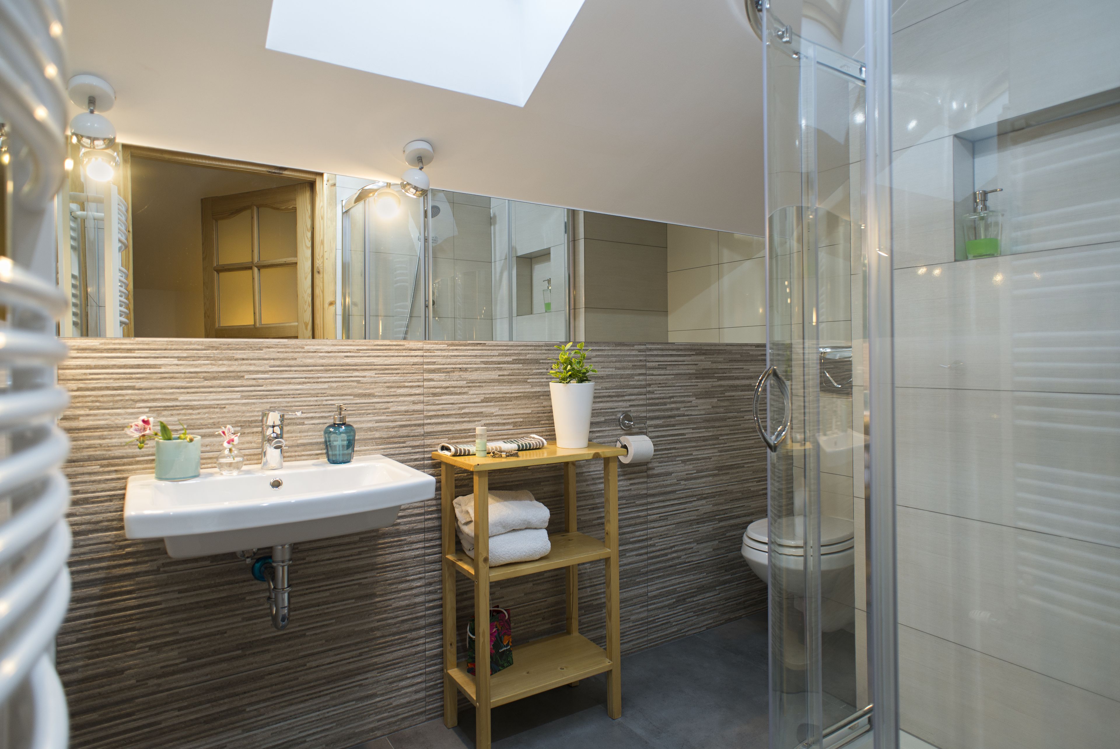 A modern bathroom with a skylight, a sink with a wooden shelf, a toilet, and a glass shower enclosure.