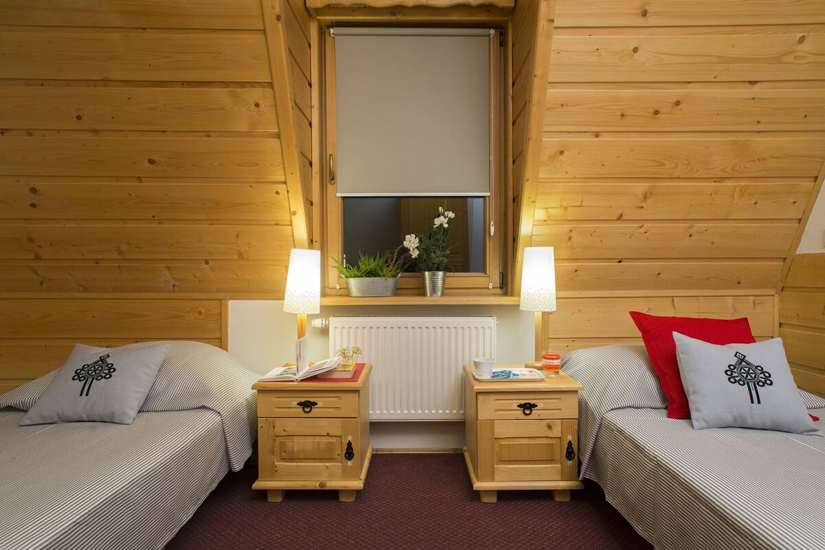 Une pièce confortable avec deux lits, des murs en bois, une fenêtre donnant sur un beau paysage, des tables de chevet avec des lampes et un radiateur.