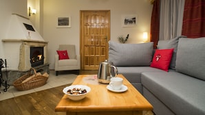 A cozy living room with a fireplace, a sofa, a coffee table, and a basket of firewood.
