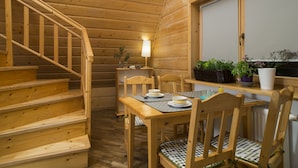 A wooden interior with a staircase, a dining table with chairs, a lamp, and potted plants.