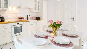A modern kitchen with white cabinetry, a wooden countertop, and a dining table set for four with pink placemats and a vase of flowers. -  Apartament Nowe Miasto - Park Róż (Gorzow Wielkopolski)