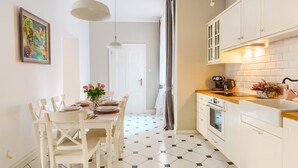 A modern kitchen with white cabinets, a wooden countertop, and a tiled floor. There is a dining table with chairs and a vase of flowers. -  Apartament Nowe Miasto - Park Róż (Gorzow Wielkopolski)