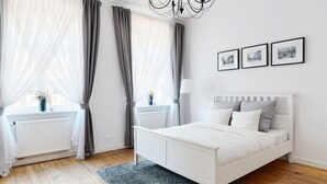 A modern bedroom with a white bed, grey curtains, and a radiator. There are three framed pictures on the wall. -  Apartament Nowe Miasto - Park Róż (Gorzow Wielkopolski)