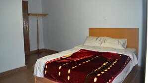 A bedroom with a bed, a wooden headboard, and a red blanket with yellow dots. - Wailers Lodge (Kigali)