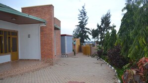 A courtyard with a paved walkway, a brick building, and a bench. - Wailers Lodge (Kigali)