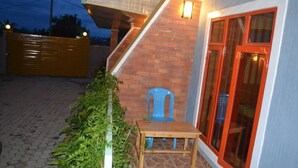 A patio with a wooden table and blue plastic chairs, a brick wall, and a glass door with red trim. - Wailers Lodge (Kigali)