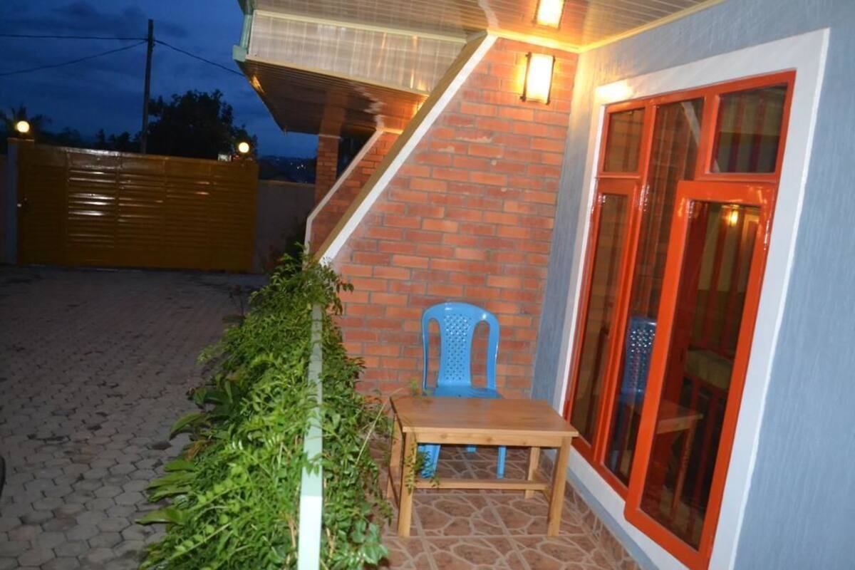 A patio with a wooden table and blue plastic chairs, a brick wall, and a glass door with red trim.