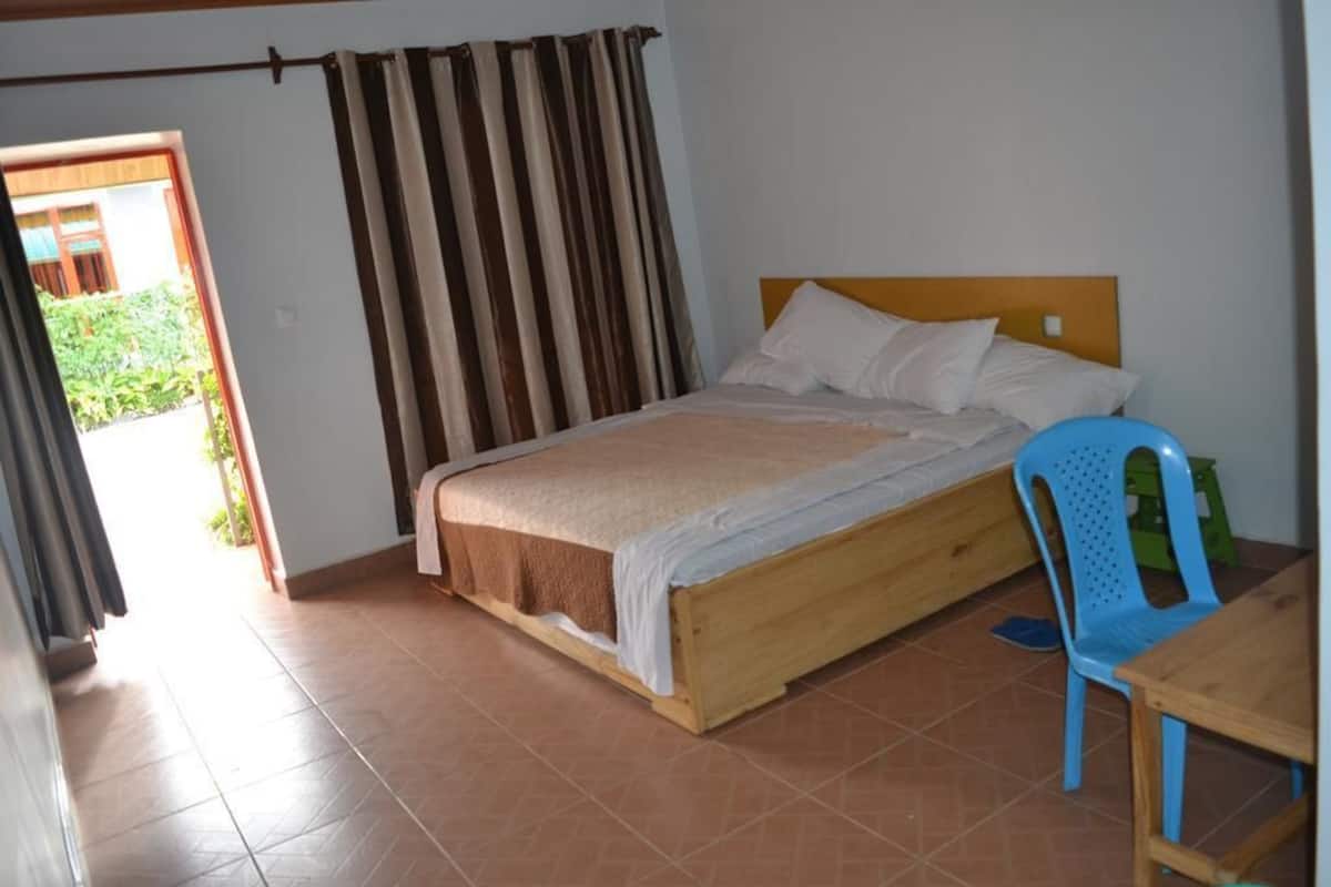 A bedroom with a wooden bed, a blue plastic chair, and a small table.