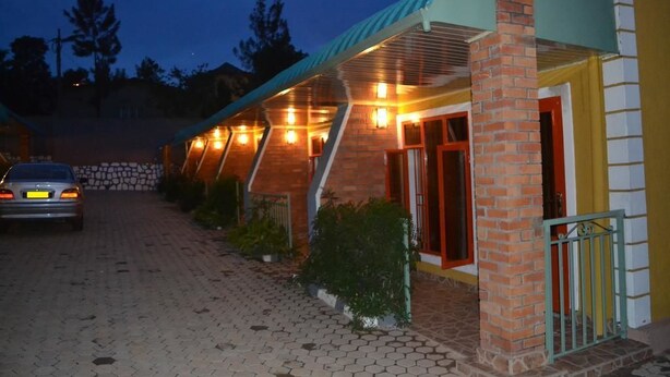 A hotel with a brick facade, multiple windows with lights, and a paved driveway. - Wailers Lodge (Kigali)