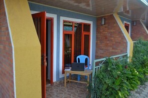 A room with a wooden door, a window with red frames, a small table with a laptop, and a chair.