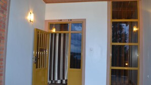 A building entrance with a yellow door, a glass door, and a window with a view of trees. - Wailers Lodge (Kigali)