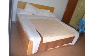 A single bed with a wooden headboard, white bedding, and a brown skirt.