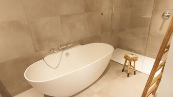 A modern bathroom with a freestanding bathtub, a glass shower enclosure, and a wooden stool.