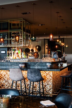 A bar area with a marble countertop, multiple hanging light fixtures, and bar stools. - Van der Valk Hotel Apeldoorn (Apeldoorn)