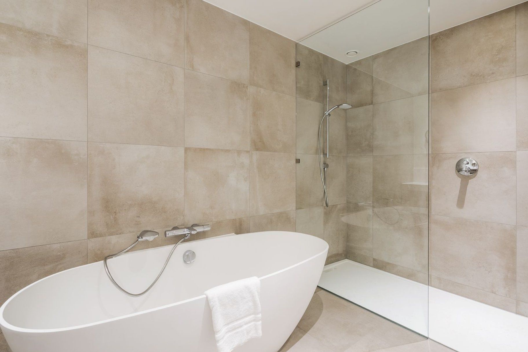 A modern bathroom with a freestanding bathtub, a glass-enclosed shower, and beige tiled walls.