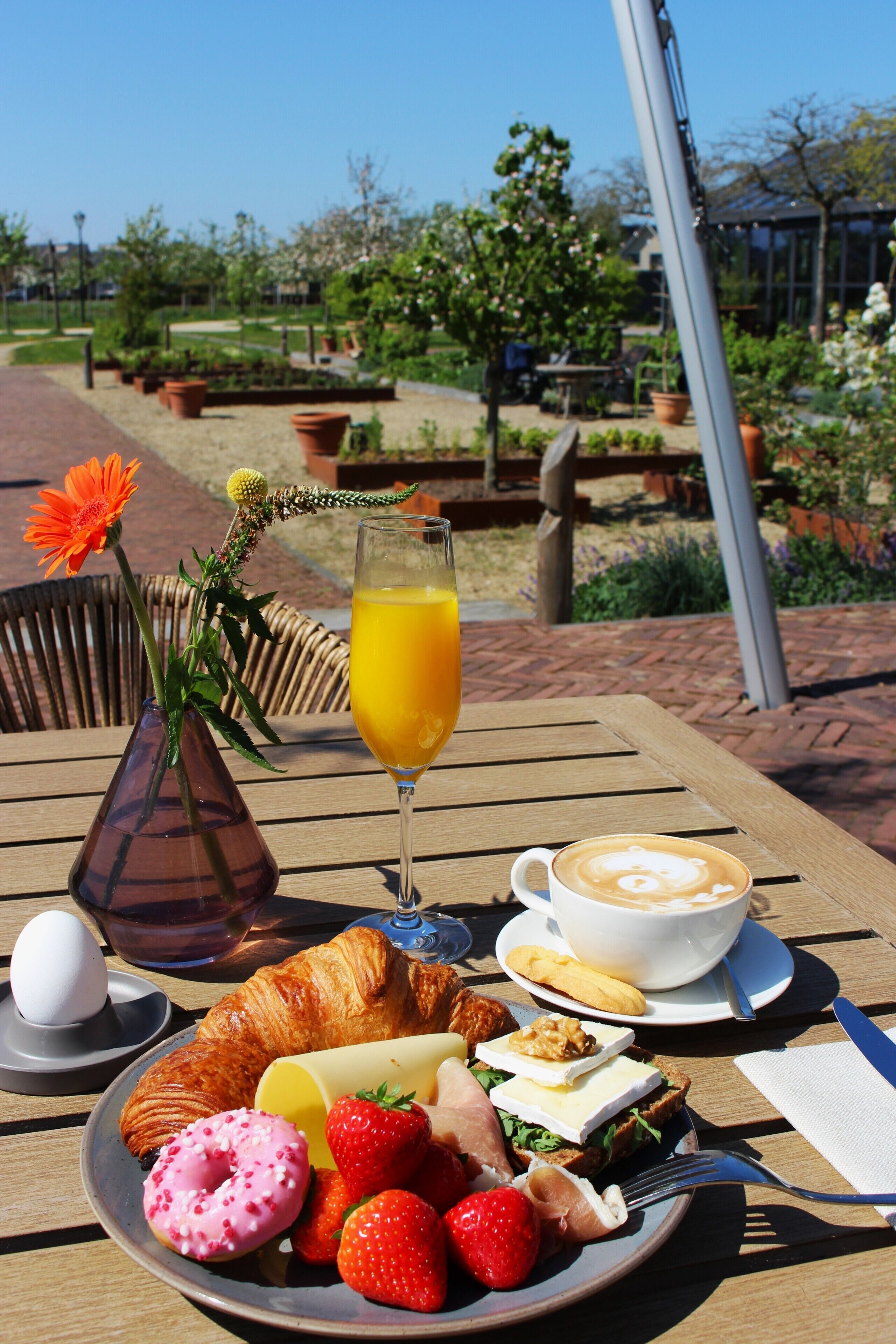 A breakfast table with croissants, strawberries, a donut, a glass of orange juice, a coffee cup, and a plate with eggs and cheese.