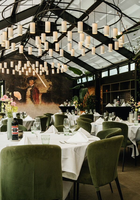 A restaurant with tables set for dining, hanging pendant lights, and a mural on the wall.