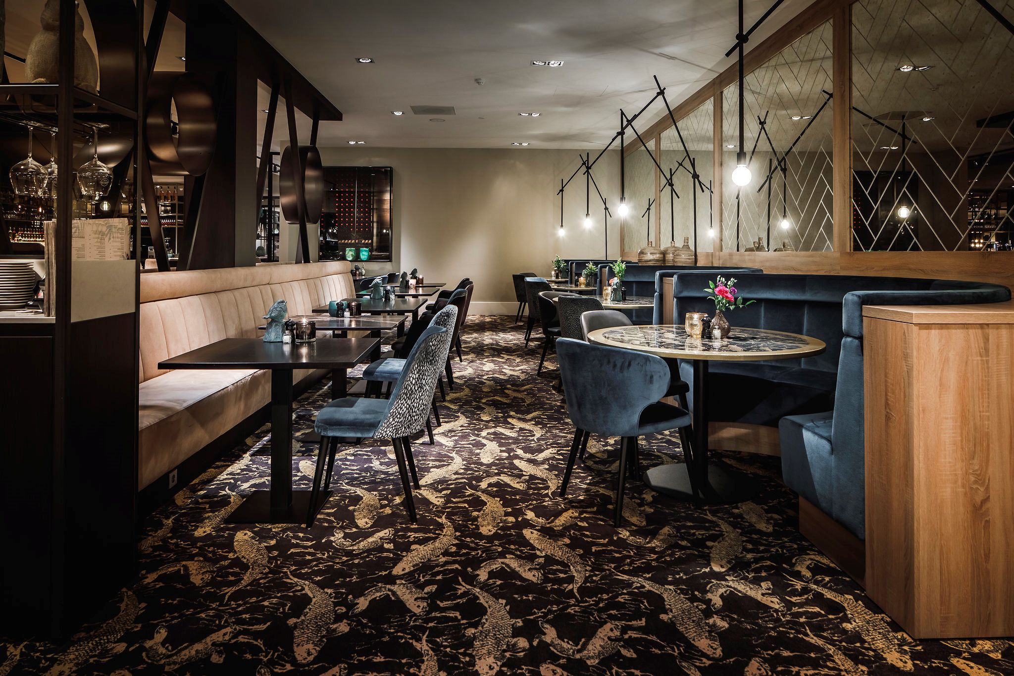 A restaurant with booths and tables, patterned carpet, and hanging lights.