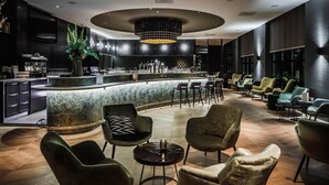 Un área de bar moderna con mostrador de mármol, taburetes y una zona de estar con sillones tapizados y una mesa redonda.