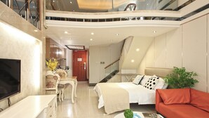 A modern hotel room with a bed, a red sofa, a TV, a dining area, and a staircase. - Badun International Apartment (Guangzhou)