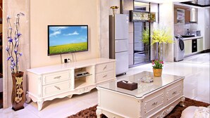 A spacious living area with a flat-screen TV, a white entertainment unit, a brown shag rug, and a kitchen in the background. - Badun International Apartment (Guangzhou)