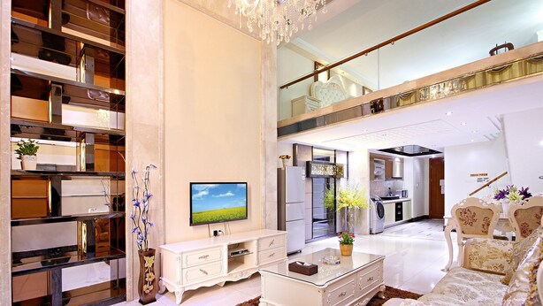 A spacious living room with a high ceiling, a large flat-screen TV, a white sofa, a coffee table, and a decorative plant. - Badun International Apartment (Guangzhou)