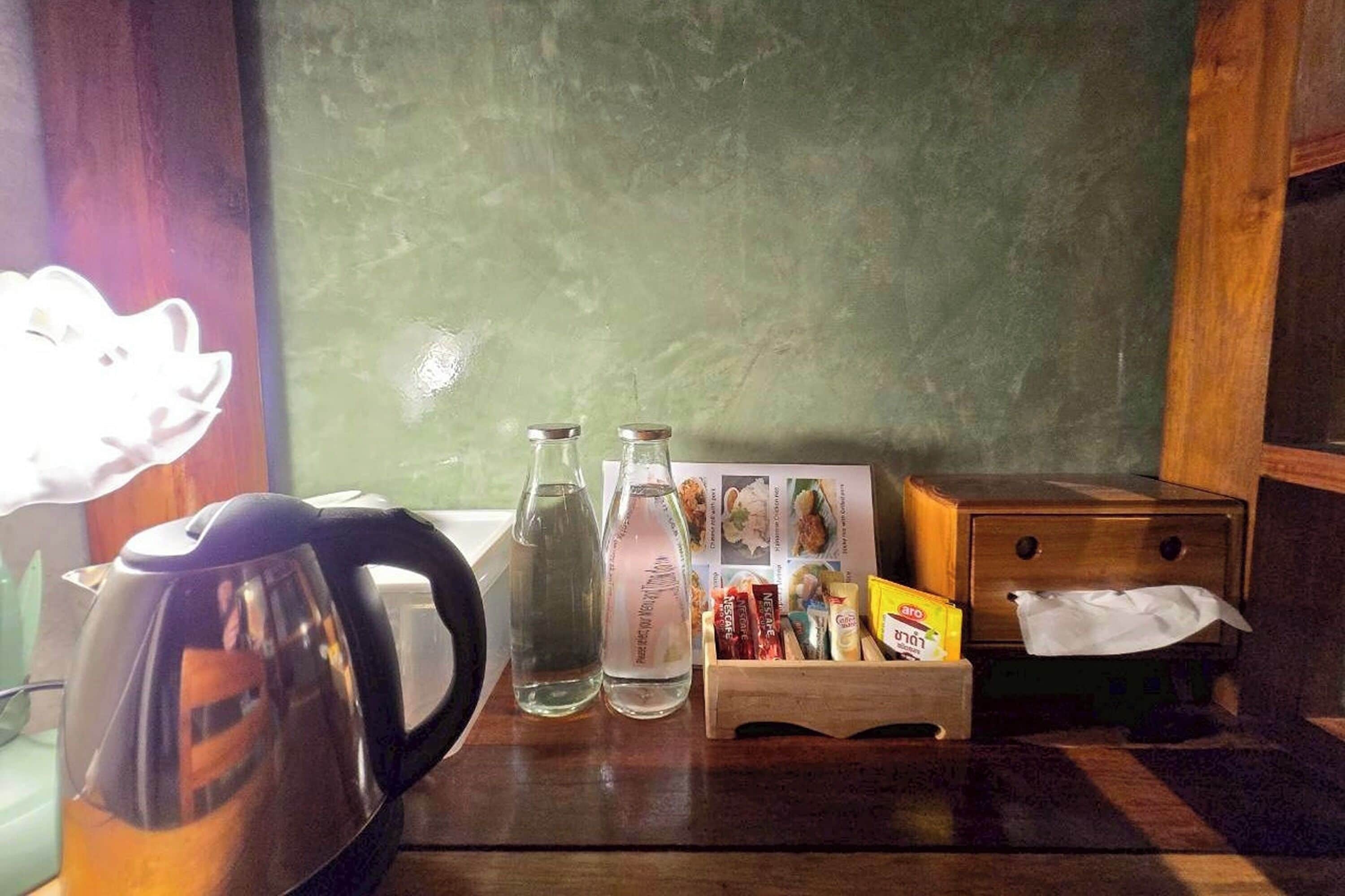 A wooden table with a kettle, two bottles, a tissue box, and a card holder with snacks.