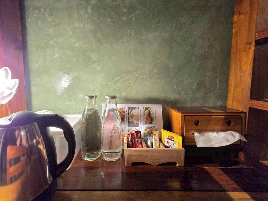 A wooden table with a kettle, two bottles, a tissue box, and a card holder with snacks.