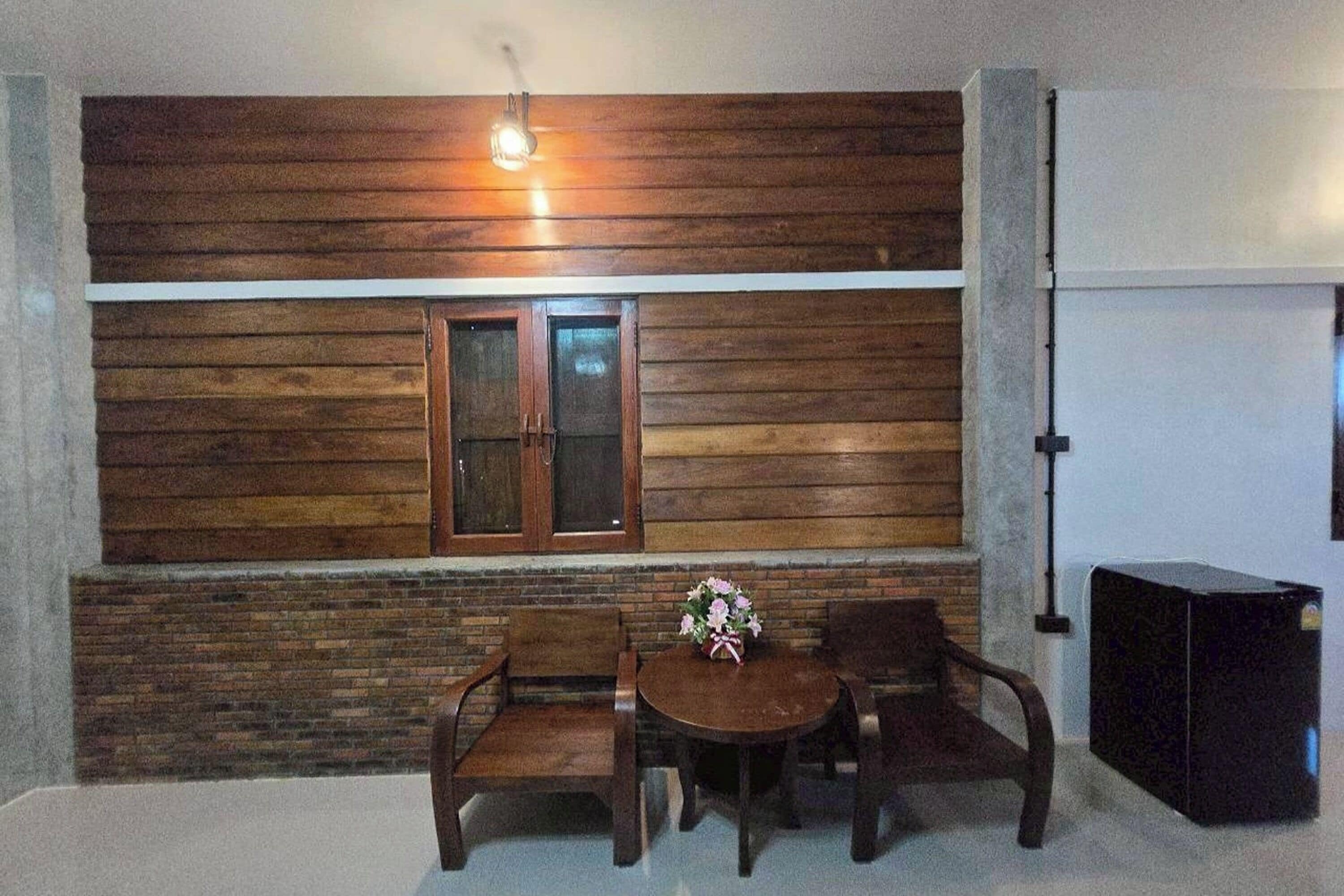 Una habitación con panel de pared de madera, una ventana que funciona como puerta, una mesa redonda con sillas y un armario negro.