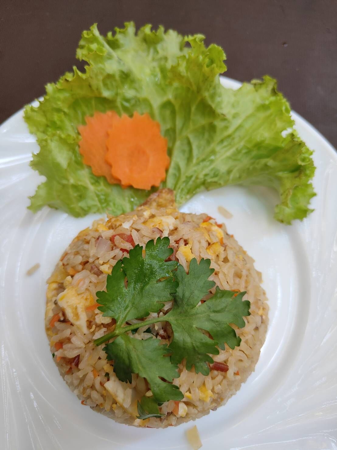 A plate of fried rice with vegetables and a garnish of cilantro, accompanied by a side of lettuce and a carrot slice.