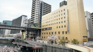 A multi-story hotel with a modern design, located near a river with a pedestrian bridge. - Hotel Royal Oak Gotanda (Tokyo)