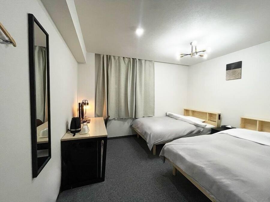 A hotel room with two single beds, a desk with a chair, a mirror, and a ceiling light.