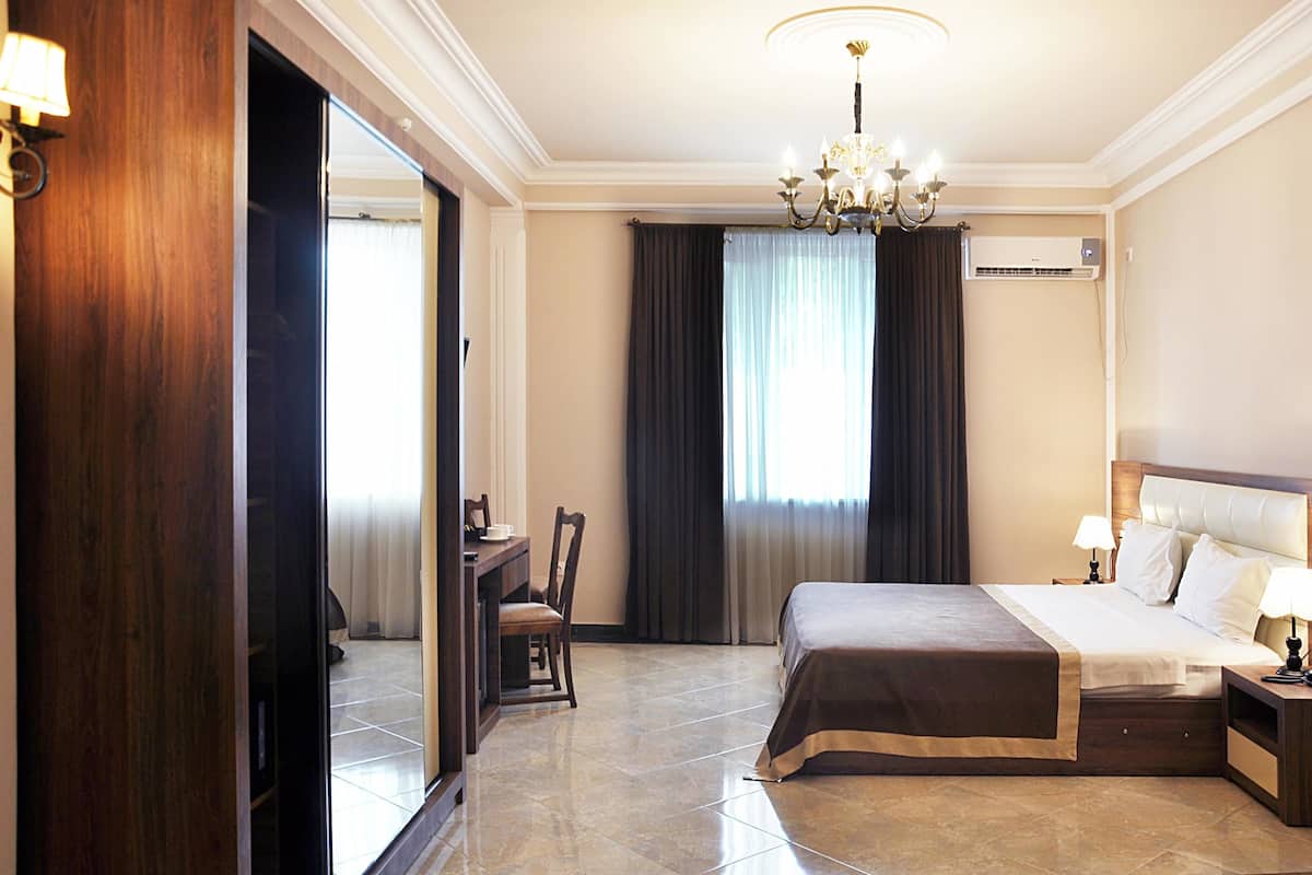 Habitación de hotel con una cama grande, un escritorio con silla, una araña y un equipo de aire acondicionado.