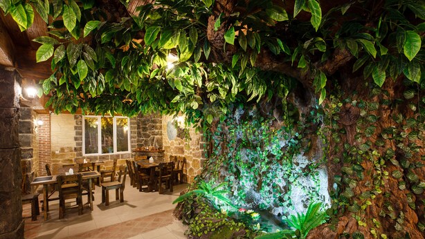 Un restaurant avec des tables et des chaises en bois, des murs en pierre et un mur de pierres recouvertes de verdure.