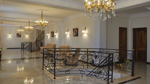 Un vaste hall d’entrée agrémenté de lustres somptueux, un espace de détente central doté d’une rampe en fer forgé et un escalier éclairé par des appliques murales.