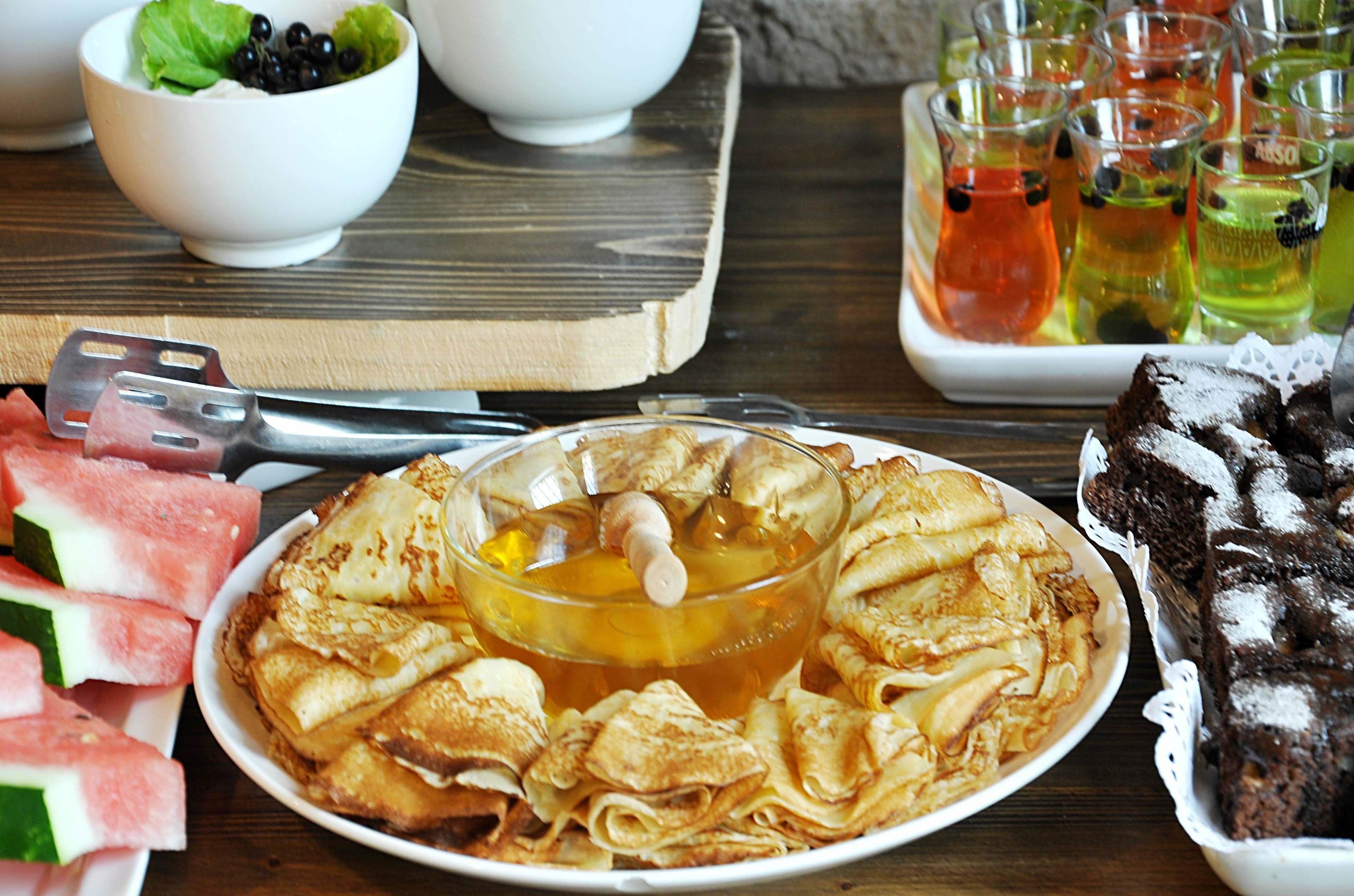 Une table garnie de différents aliments, notamment des crêpes, des tranches de pastèque et un dessert.