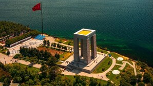 Vista aérea de una zona costera con un edificio cuadrado destacado, una bandera y una vista despejada del mar.