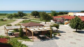 Un espacio al aire libre cubierto con mesas y sillas, un camino que lleva a un edificio y vista al mar.
