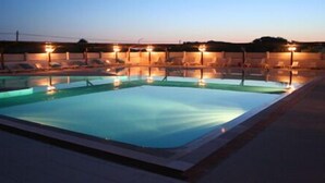 Una piscina rectangular con sillas de descanso e iluminación alrededor del borde.