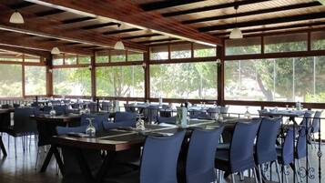 A restaurant with multiple tables and chairs, large windows, and a wooden ceiling.