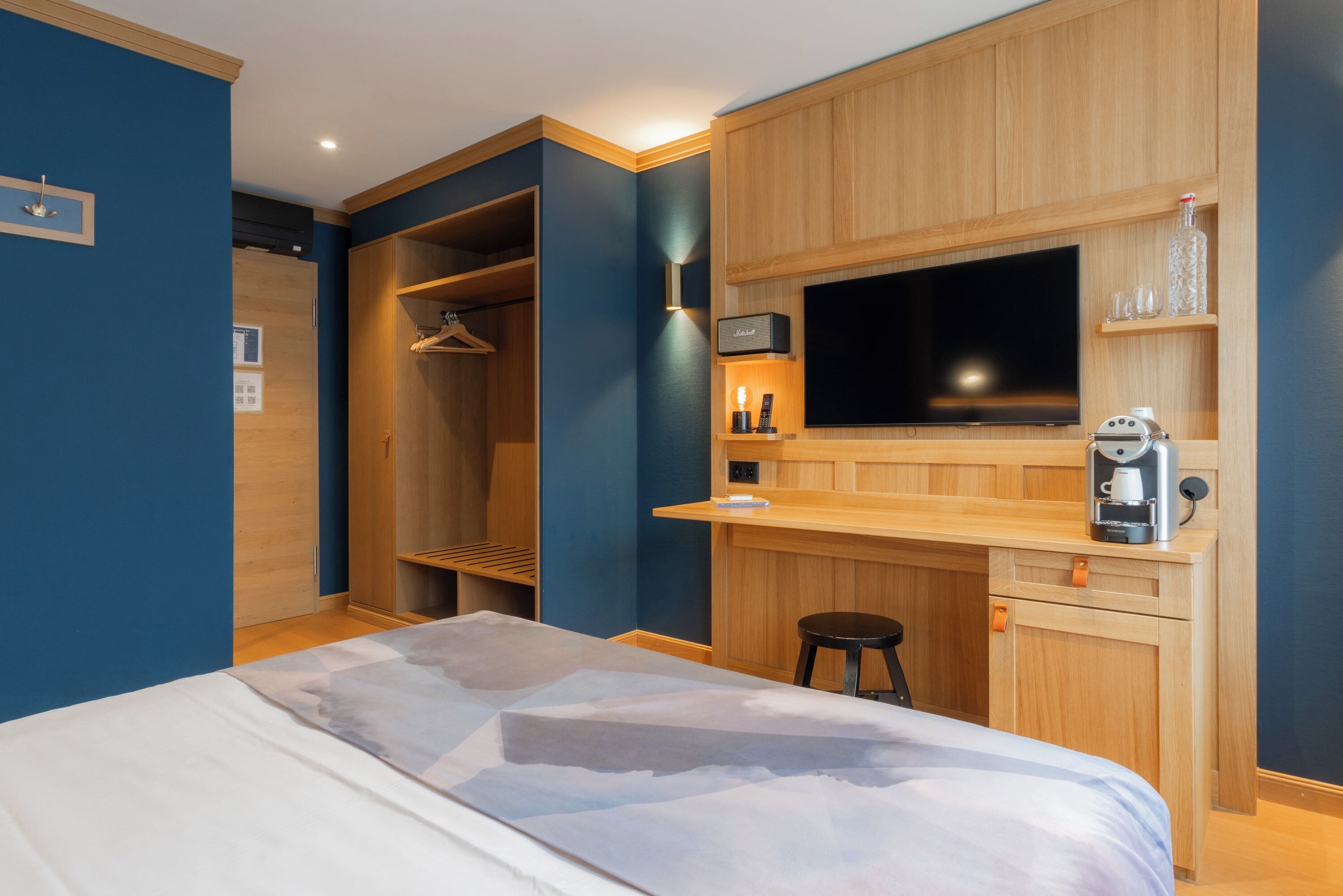 A hotel room with a bed, a wooden desk, a television, a coffee maker, and a wardrobe.