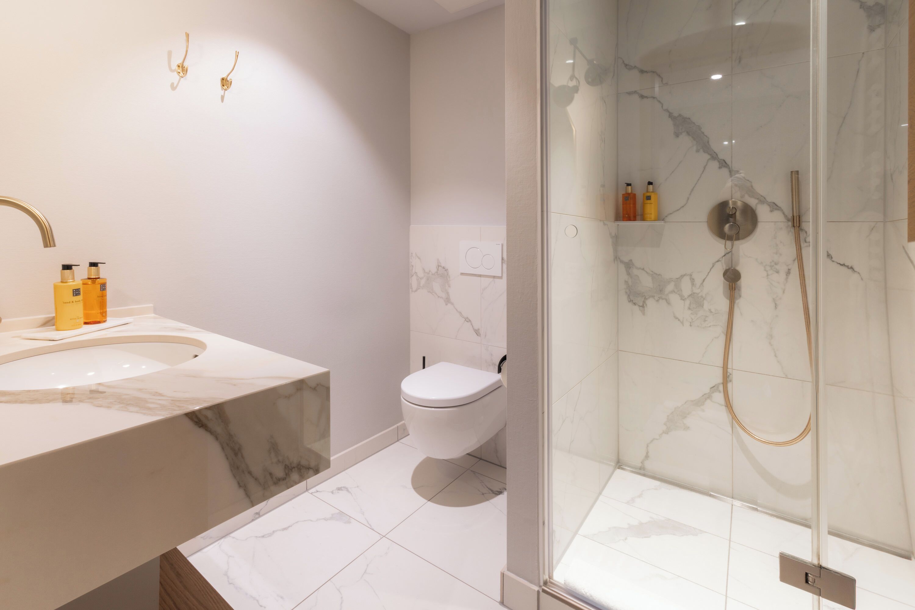 A modern bathroom with a marble sink, toilet, and glass-enclosed shower.