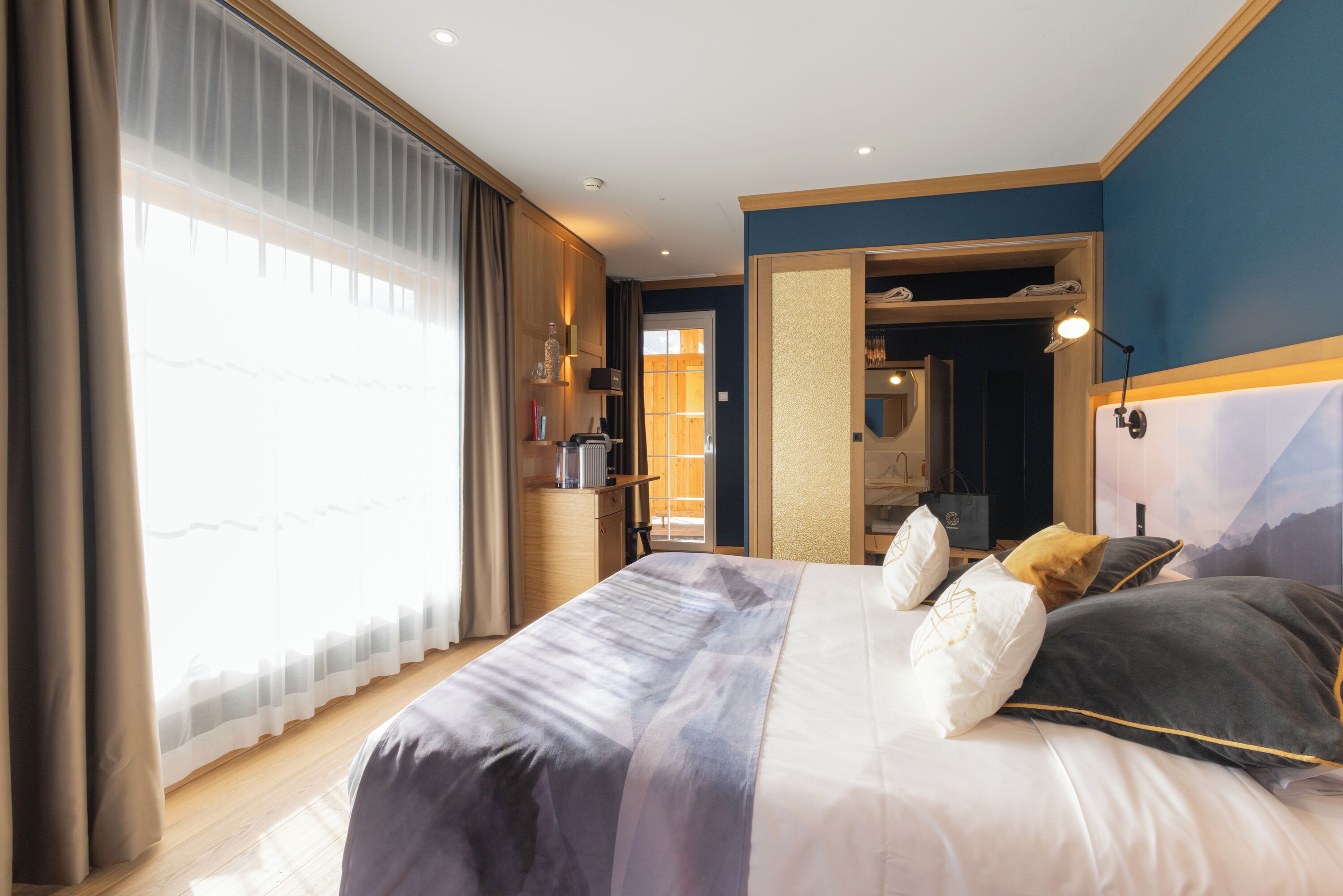 Un dormitorio con una cama grande, un armario, un escritorio y un baño visible a través de una puerta abierta.