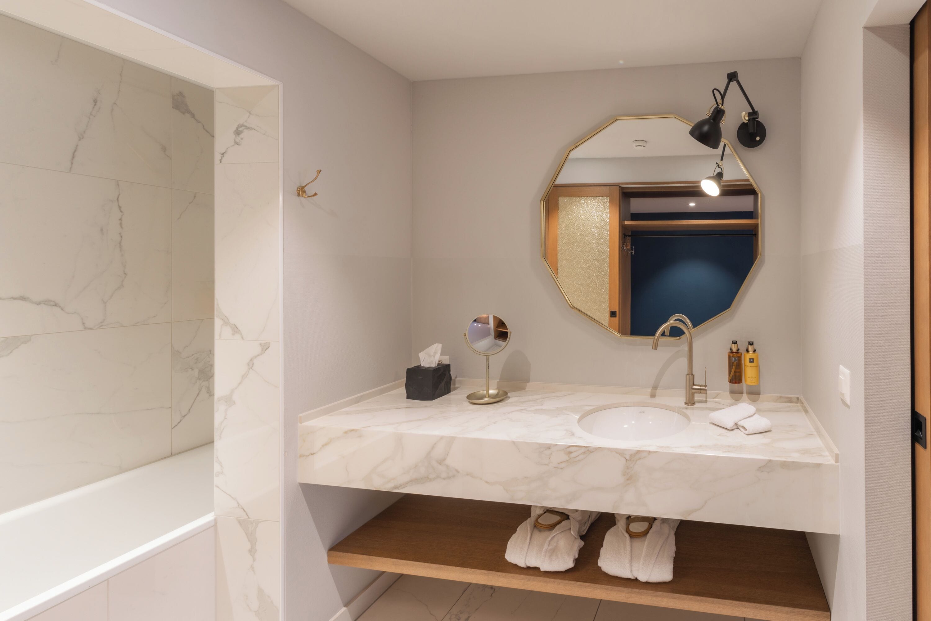 A bathroom with a marble sink, a round mirror, and a towel rack.