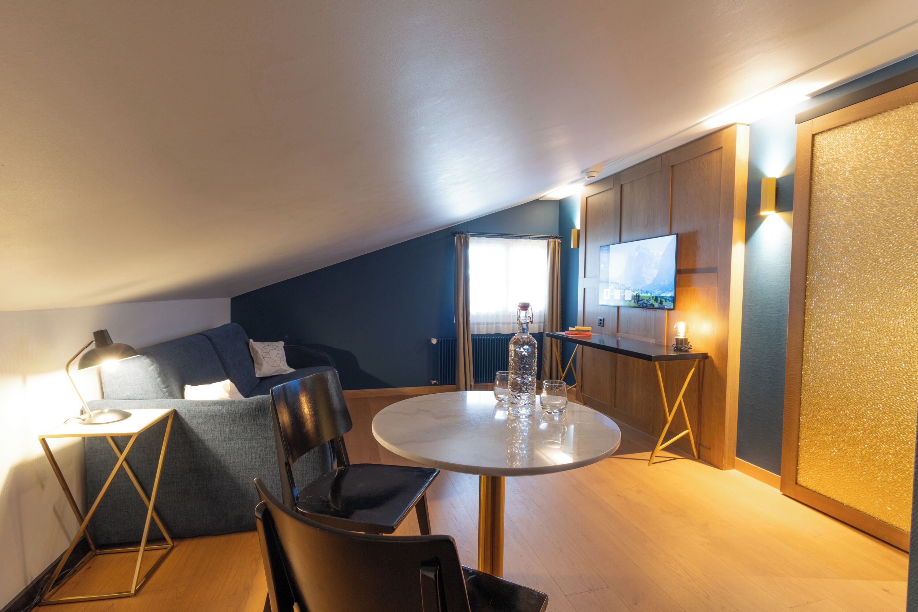A cozy room with a round table, a sofa, a TV, and a kitchen area.