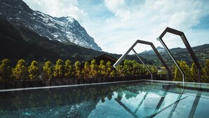 Une piscine aux eaux cristallines, avec une chaîne de montagnes en toile de fond, entourée d’arbres et d’une clôture en bois.